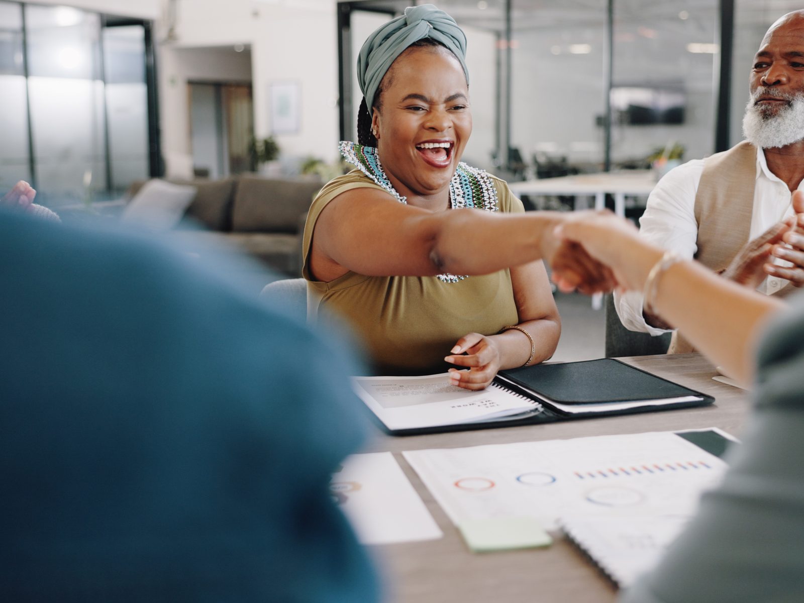 Fundraiser smiling and shaking hands across a meeting table with printed reports spread out in front of her