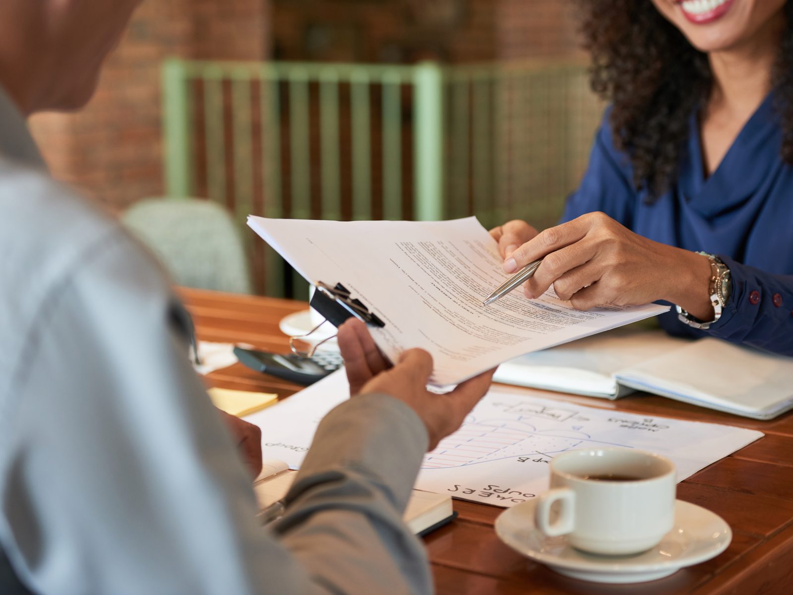 Paralegal pointing out a line in a document to a client across a table with a clipboard and coffee cup