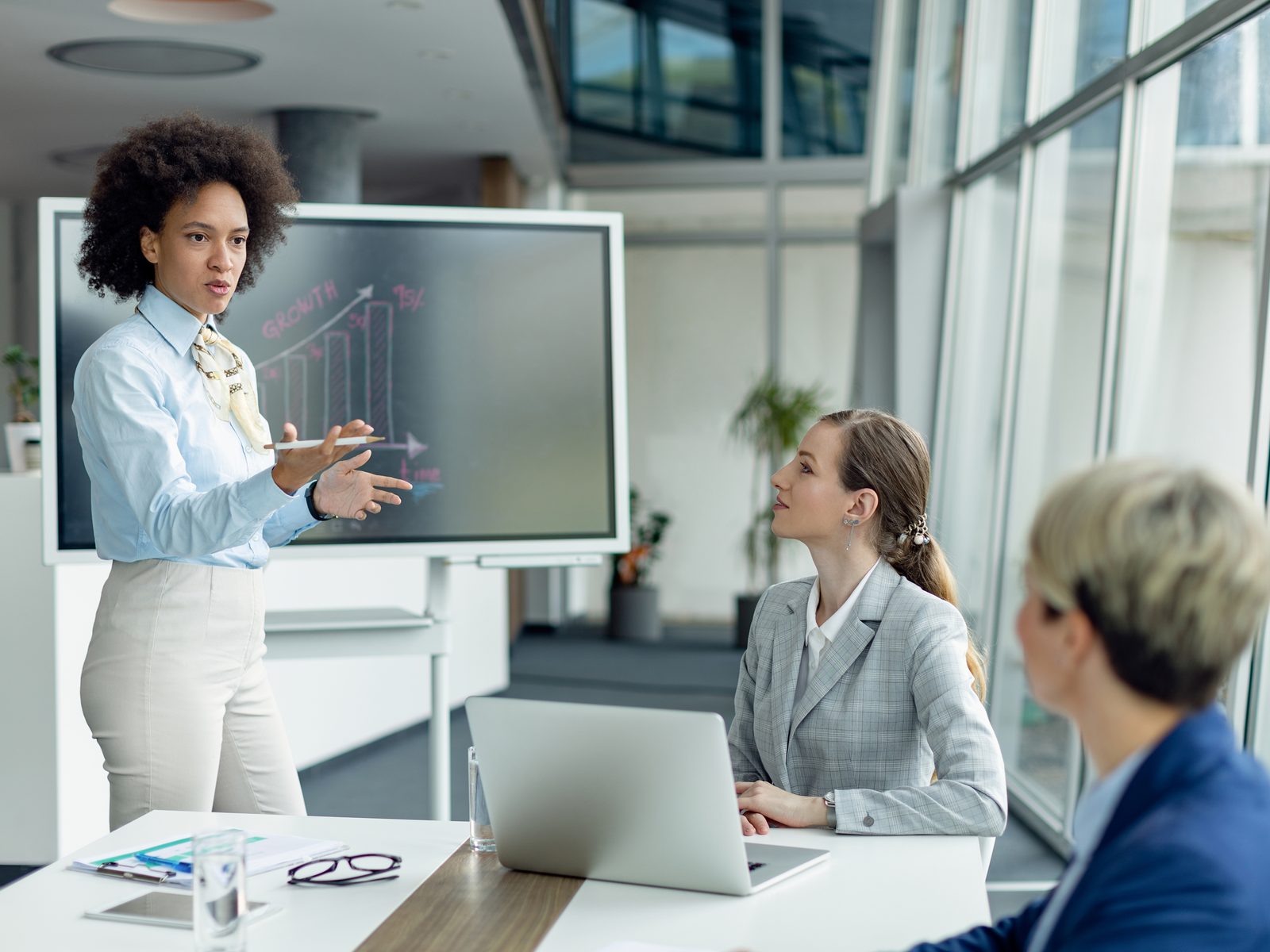 Training and development specialist presenting a growth chart on a screen to two colleagues in a meeting room