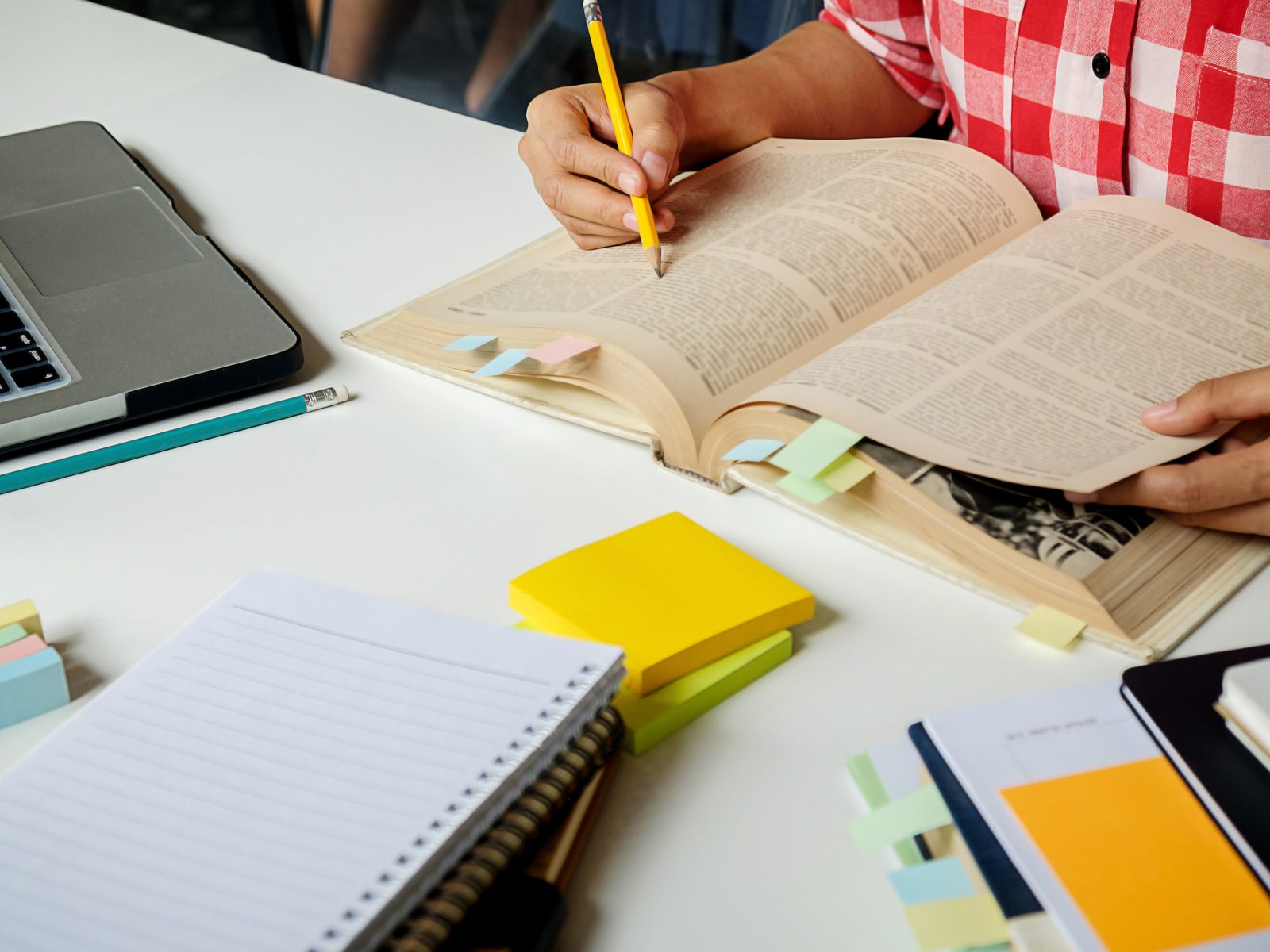 Student marking a textbook with a pencil beside a laptop and sticky notes while comparing general studies degree rankings