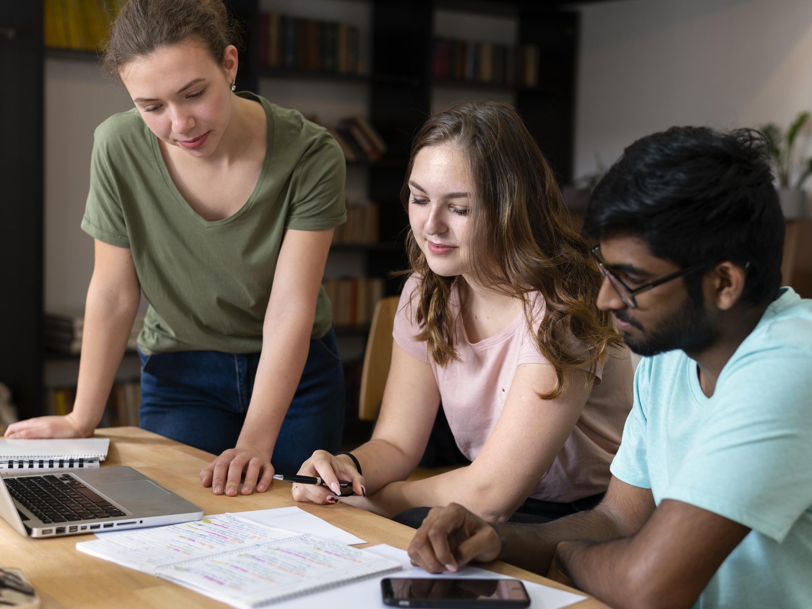 Three graduate students reviewing notes and a laptop together in a master's program in liberal studies