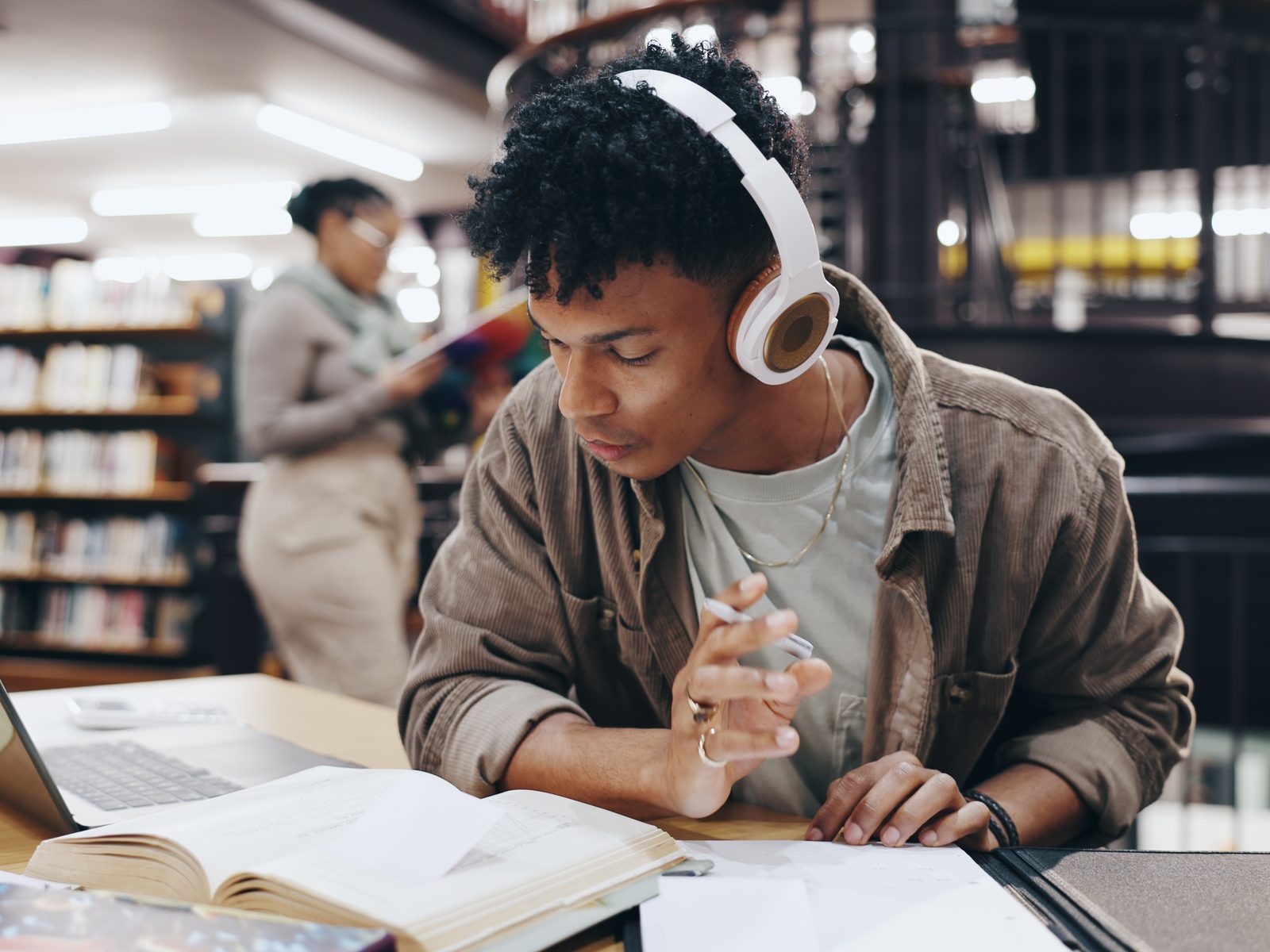 Student wearing headphones reading beside a laptop in a library, studying for an online bachelor's degree in general studies